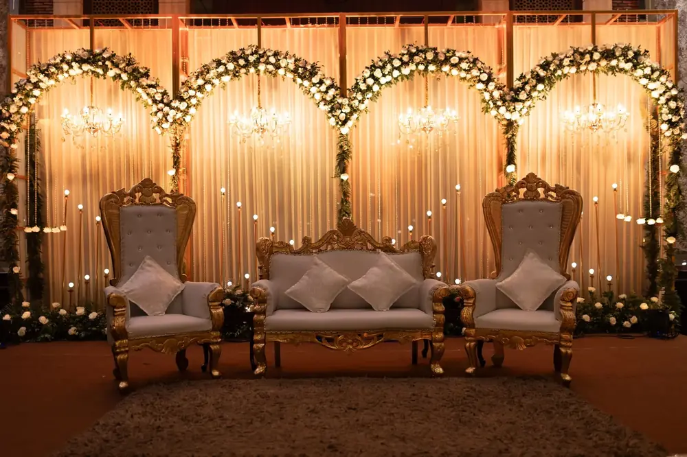 Wedding stage with lit floral arches and gold seating
